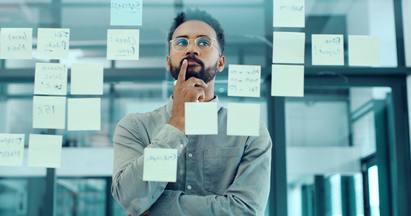 Thoughtful professional reviewing notes on a glass wall, reflecting on complex decisions and ethical considerations in compliance and risk management.